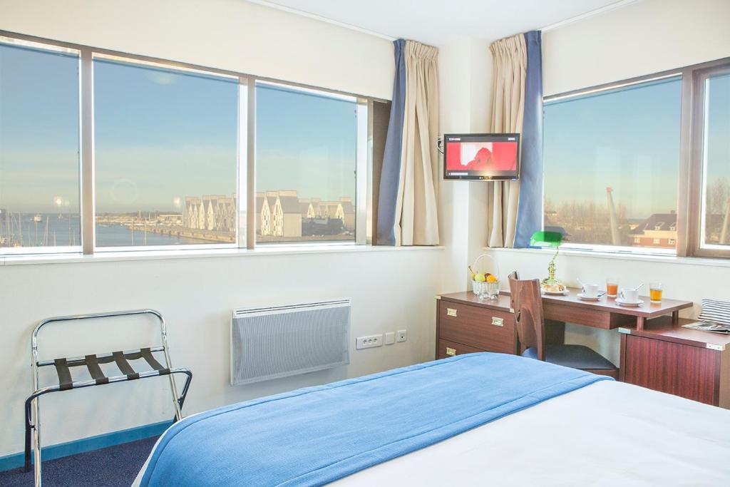 a bedroom with a bed and a desk and windows at Hôtel Les Gens De Mer Dunkerque by Popinns in Dunkerque