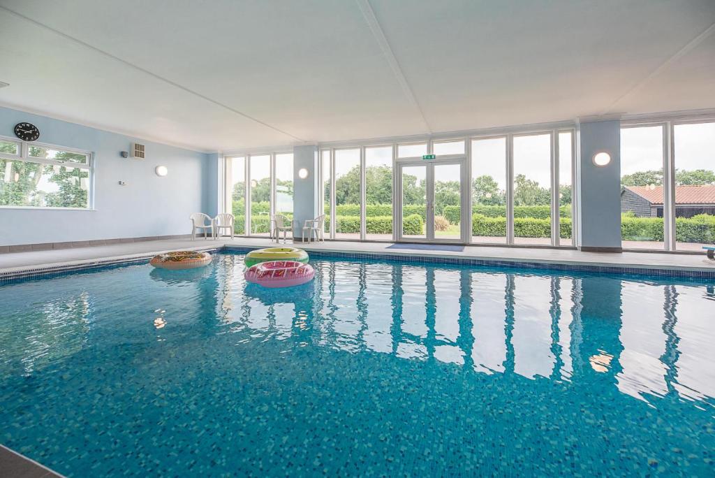 een groot zwembad met blauw water in een gebouw bij Grove Farm Bungalow with swimming pool Dallinghoo in Woodbridge