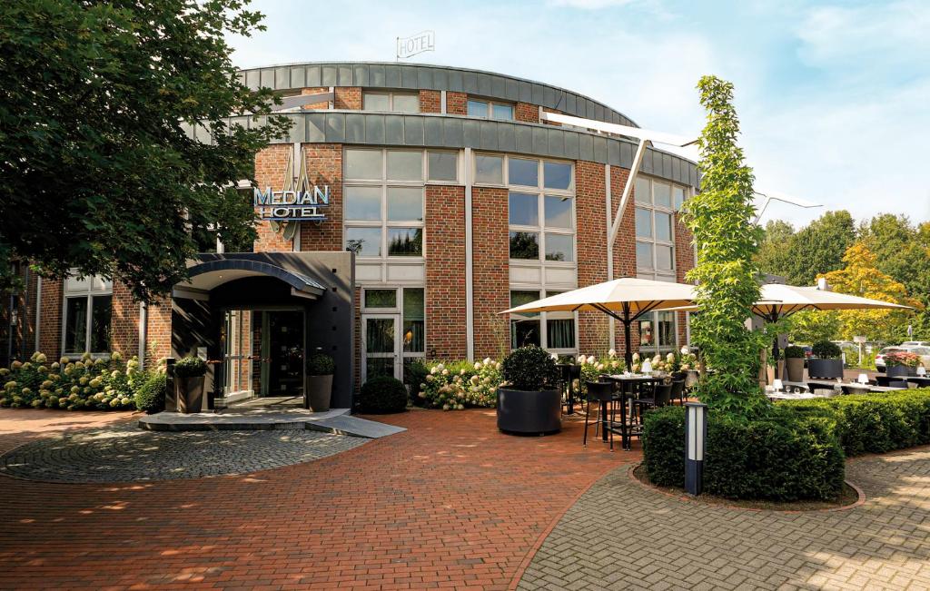 a building with tables and umbrellas in front of it at Median Hotel Hannover Lehrte in Lehrte