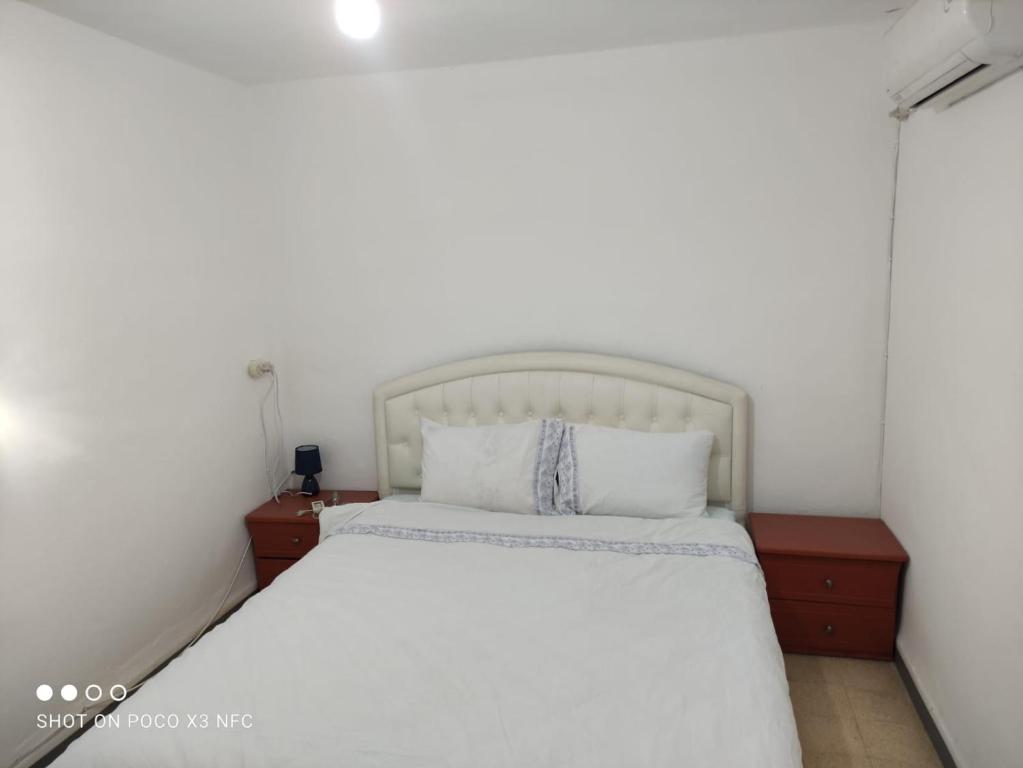 a bedroom with a white bed and two night stands at vacation house דירת אירוח פרטית 3 חדרים עפולה in El ‘Affūle