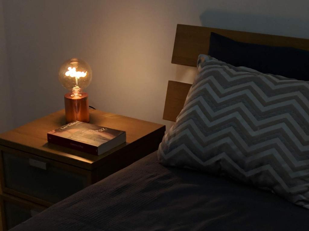 Cama con mesita de noche con lámpara y libro en Apartamento do Paço do Lumiar en Lisboa