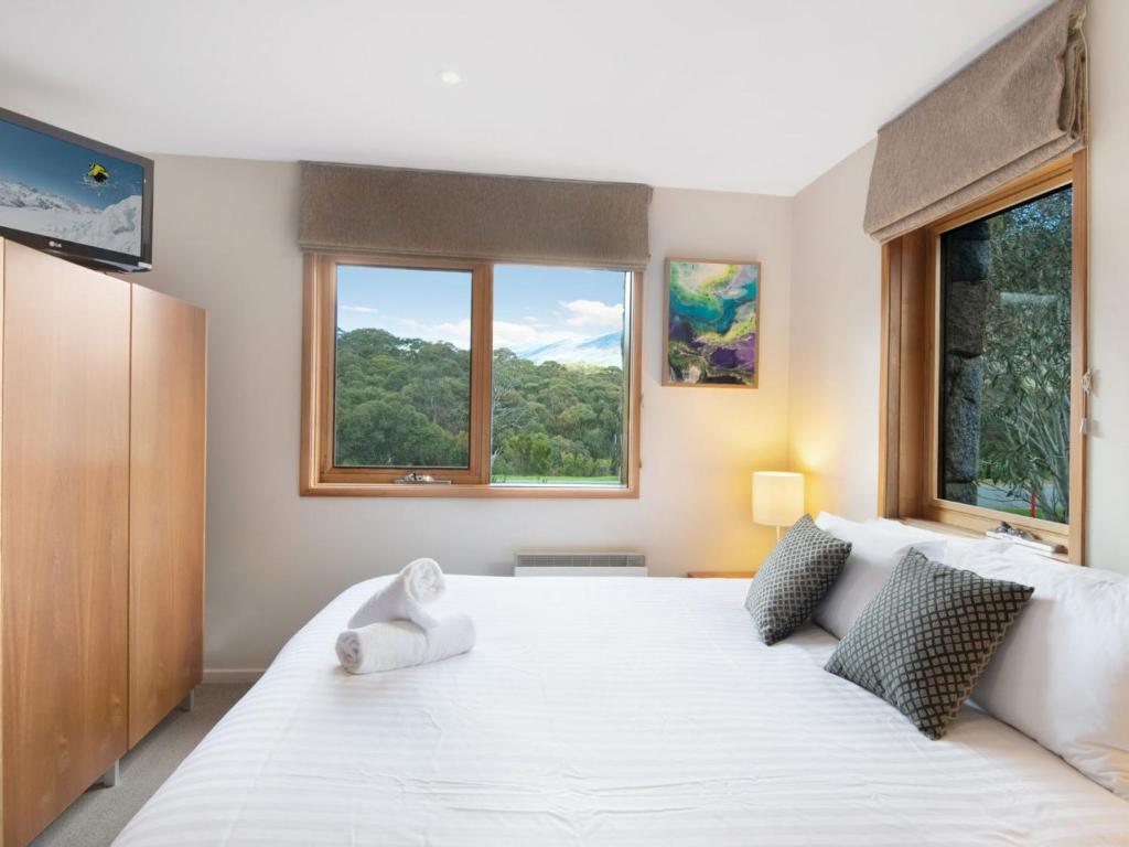 a bedroom with a large white bed with two windows at Les Perrieres Studio in Crackenback