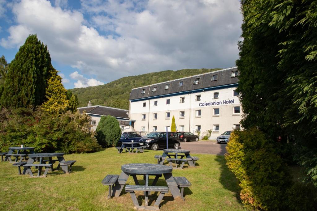 un grupo de mesas de picnic frente a un edificio en The Caledonian Hotel en Fort William