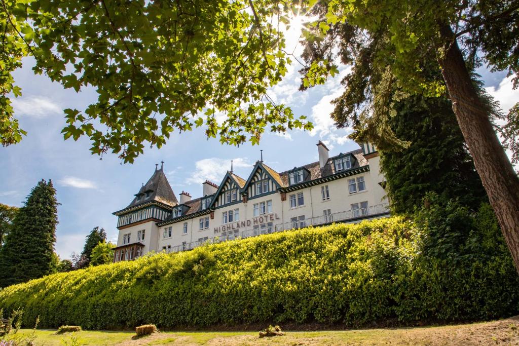 un grand château blanc sur une colline plantée d'arbres dans l'établissement The Highland Hotel by Compass Hospitality, à Strathpeffer