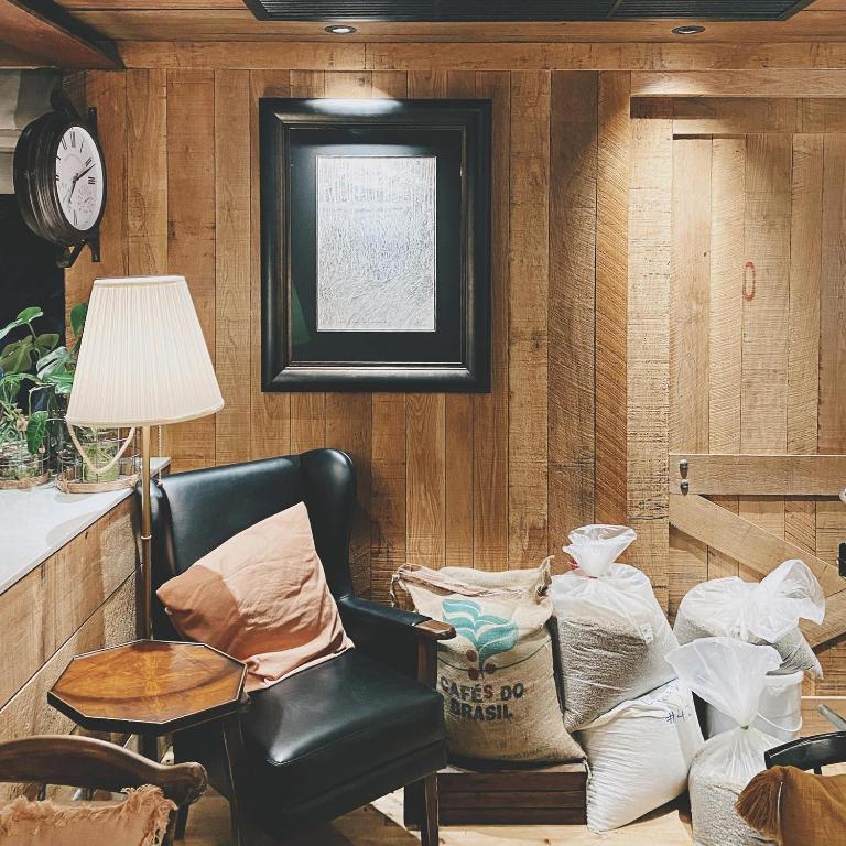 A wood-paneled sitting corner with a black leather armchair, lamp, side table and stacked sacks.