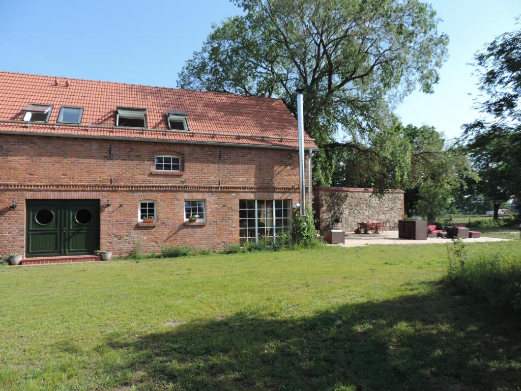 un edificio de ladrillo con una puerta verde y un campo de césped en Ferienhaus Ferienscheune Kümmernitztal en Grabow