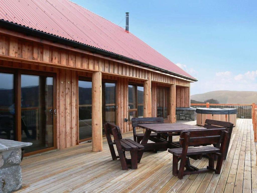 um deque de madeira com uma mesa de piquenique e bancos em Red Kite & Osprey Lodges em Rhilochan