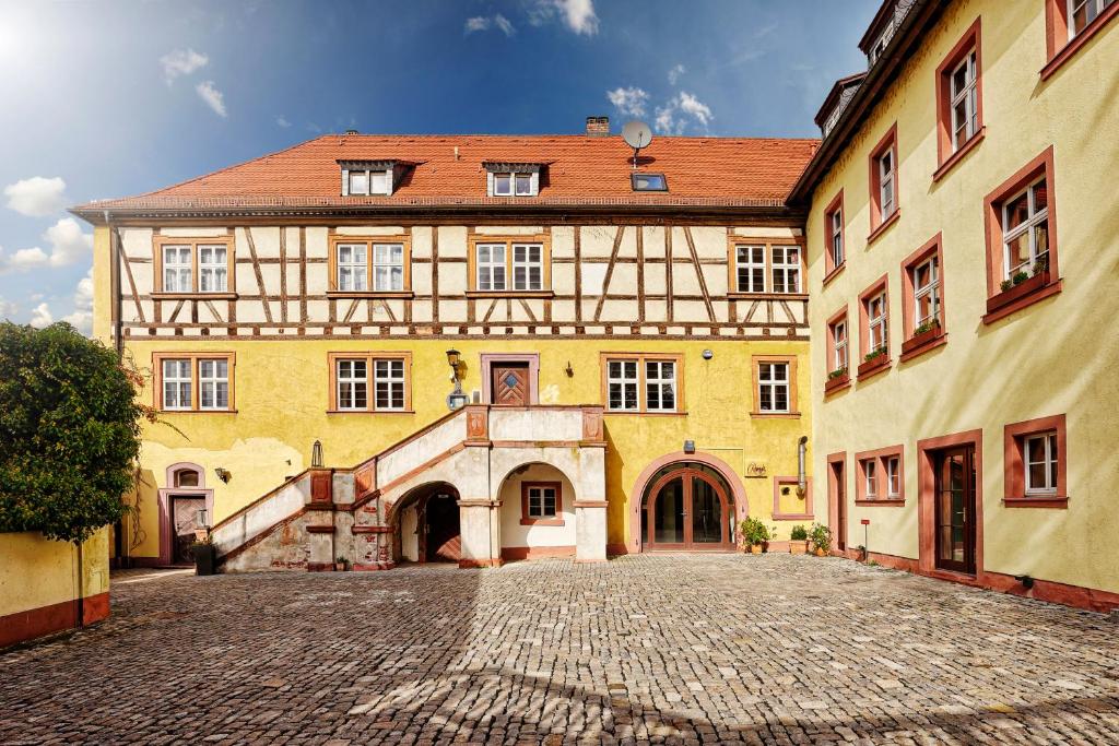 a large yellow building with a cobblestone street at HOTEL WIENER BOTSCHAFT Veitshöchheim - by homekeepers in Veitshöchheim