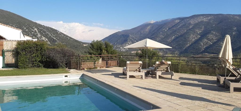- une piscine avec des chaises, un parasol et des montagnes dans l'établissement Le Ventoux, à Mollans-sur-Ouvèze