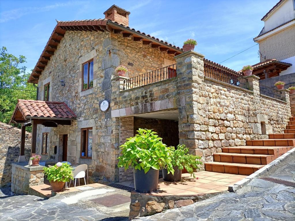 uma grande casa de pedra com escadas e plantas em frente em Apartamentos rurales La Casa Vieja De Alceda em Alceda