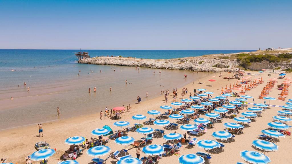 a beach with a bunch of blue and white umbrellas at Villaggio Baia della Tufara in Vieste