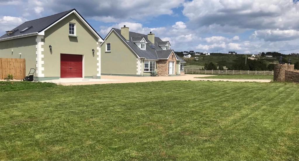 een wit huis met een rode garage in een tuin bij Ocean View in Gweedore