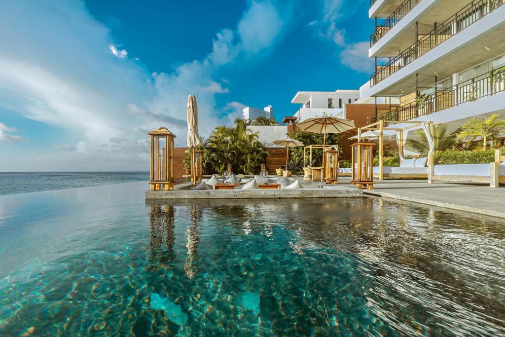 a swimming pool in front of a building with the ocean at Hotel B Unique in Cozumel