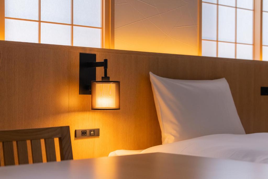 a bedroom with a bed and a lamp and windows at Tosei Hotel Cocone Kamakura in Kamakura
