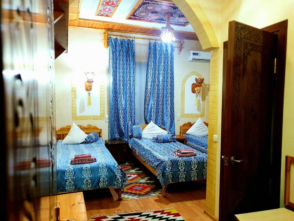 two beds in a room with blue curtains and a doorway at Zukhro Boutique Hotel in Khiva