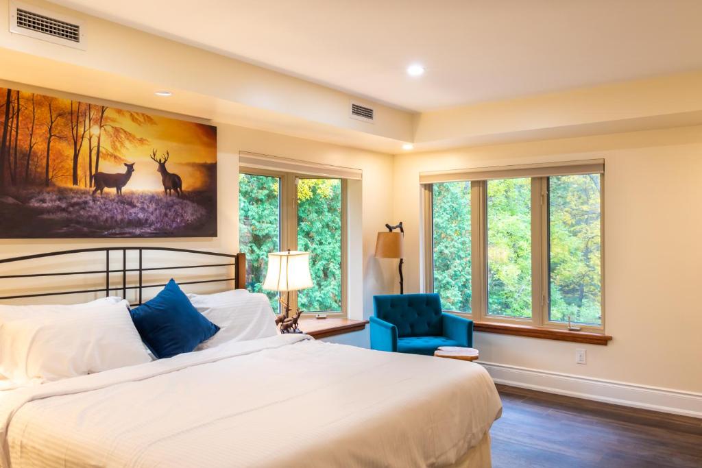 a bedroom with a bed and a blue chair and windows at Fairy Bay Lakehouse in Huntsville