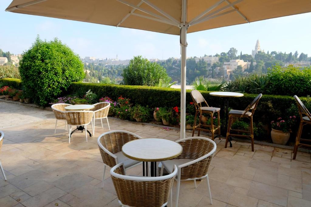 eine Terrasse mit Tischen, Stühlen und einem Sonnenschirm in der Unterkunft St Andrews Guest House in Jerusalem