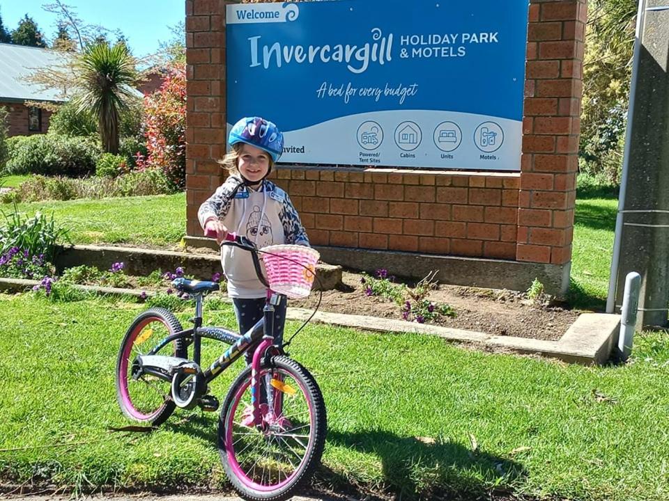 Una bambina sta in piedi accanto a una bicicletta di Invercargill Holiday Park & Motels a Invercargill