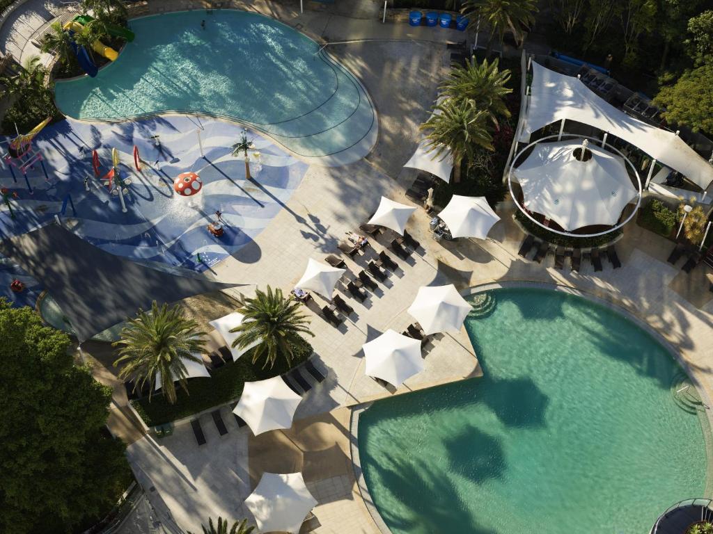 a beach with a pool, chairs, tables and umbrellas at RACV Royal Pines Resort Gold Coast in Gold Coast