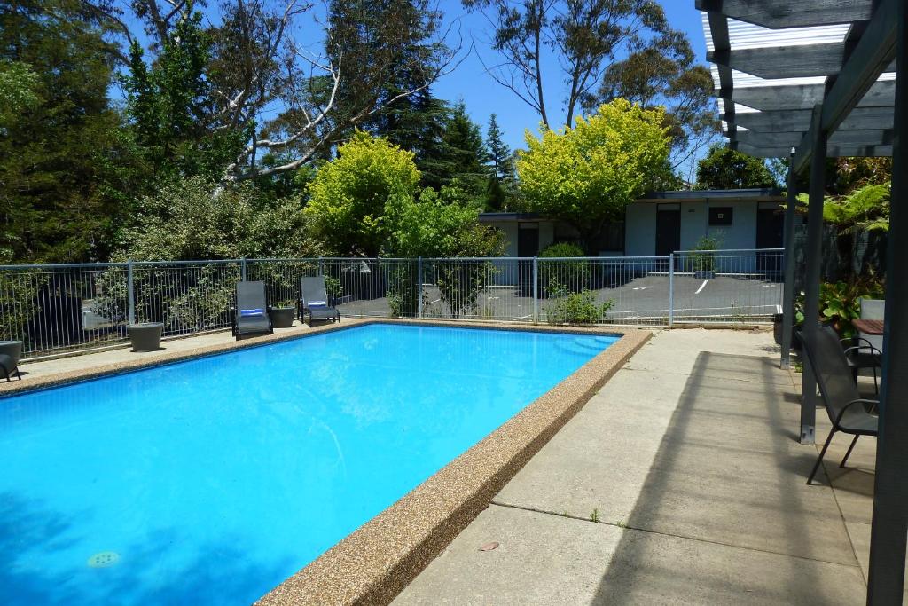 a blue swimming pool with chairs and a fence at Sky Rider Motor Inn in Katoomba