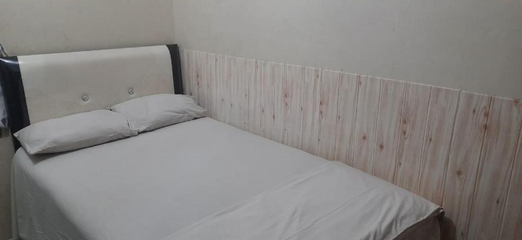 1 cama blanca con cabecero de madera en una habitación en OYO 90706 Kost Alam Jaya Syariah en Karawang