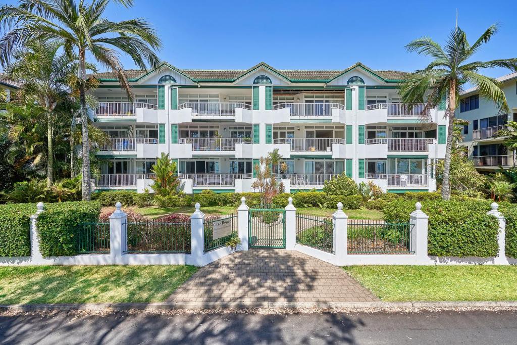 a large building with a fence and palm trees at Costa Royale Beachfront Apartment in Trinity Beach