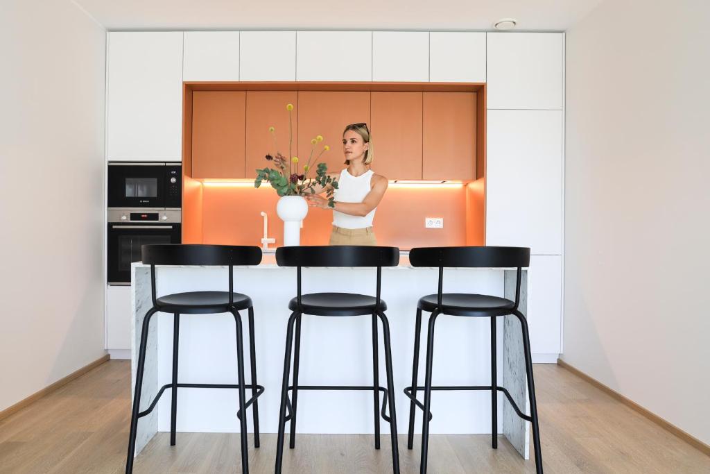 a woman standing behind a kitchen counter with four bar stools at Kadriorg Plaza 2 bedroom FREE Parking in Tallinn