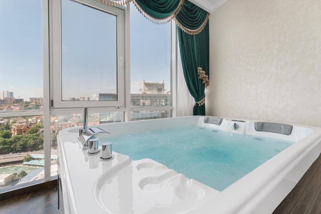Arcadia Plaza Apartments في أوديسا: حوض استحمام كبير في حمام مع نافذة كبيرة