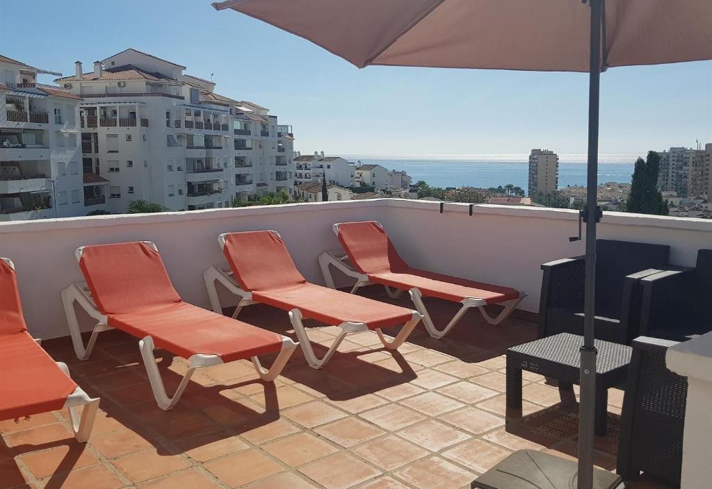 balkon z pomarańczowymi krzesłami i parasolem w obiekcie Penthouse at Pueblo Evita w mieście Benalmádena