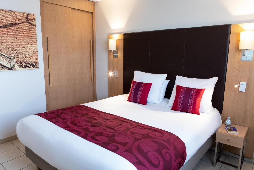 a hotel room with a large white bed with red pillows at Residhome Toulouse Occitania in Toulouse