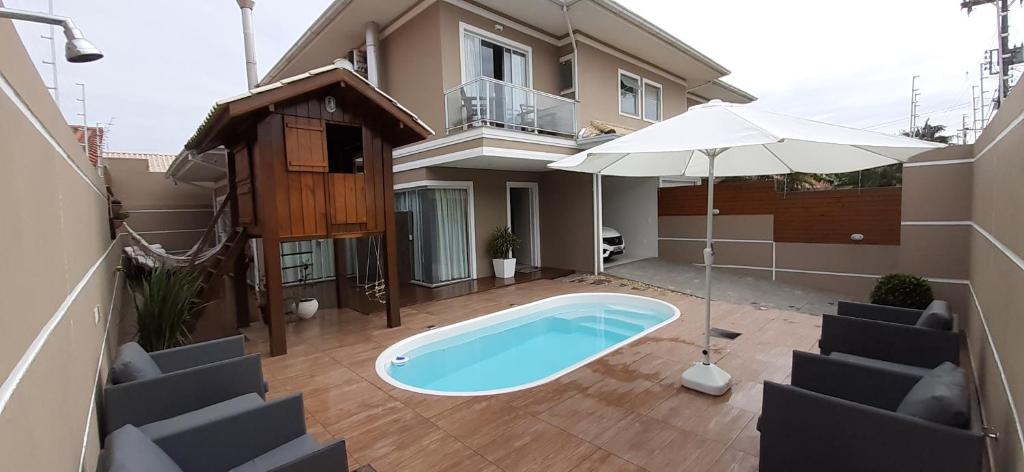 una piscina frente a una casa con sombrilla en Casa de Praia em PONTA DAS CANAS, FLORIANÓPOLIS, en Florianópolis