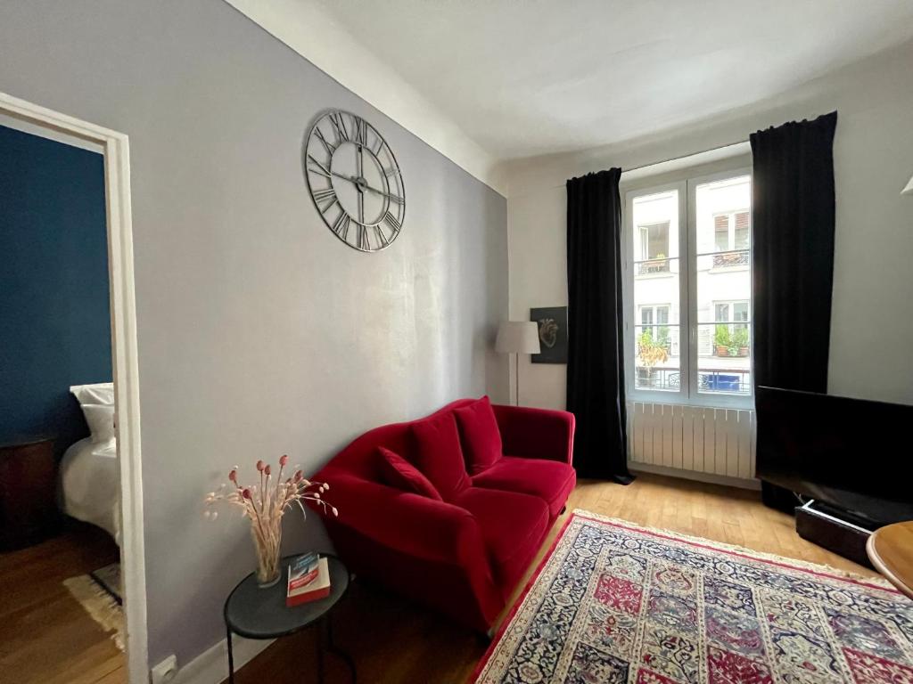 un salon avec une chaise rouge et une horloge murale dans l'établissement Maison de ville cosy Canal Saint Martin, à Paris