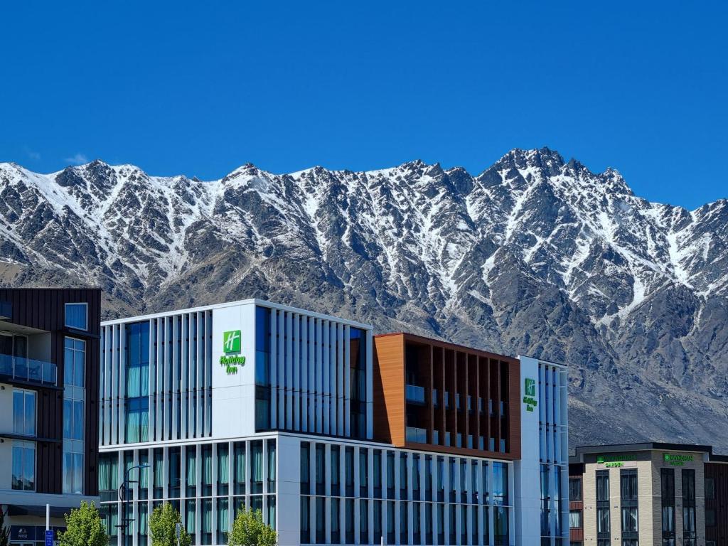 a building with snow covered mountains in the background at Holiday Inn Queenstown Remarkables Park in Queenstown