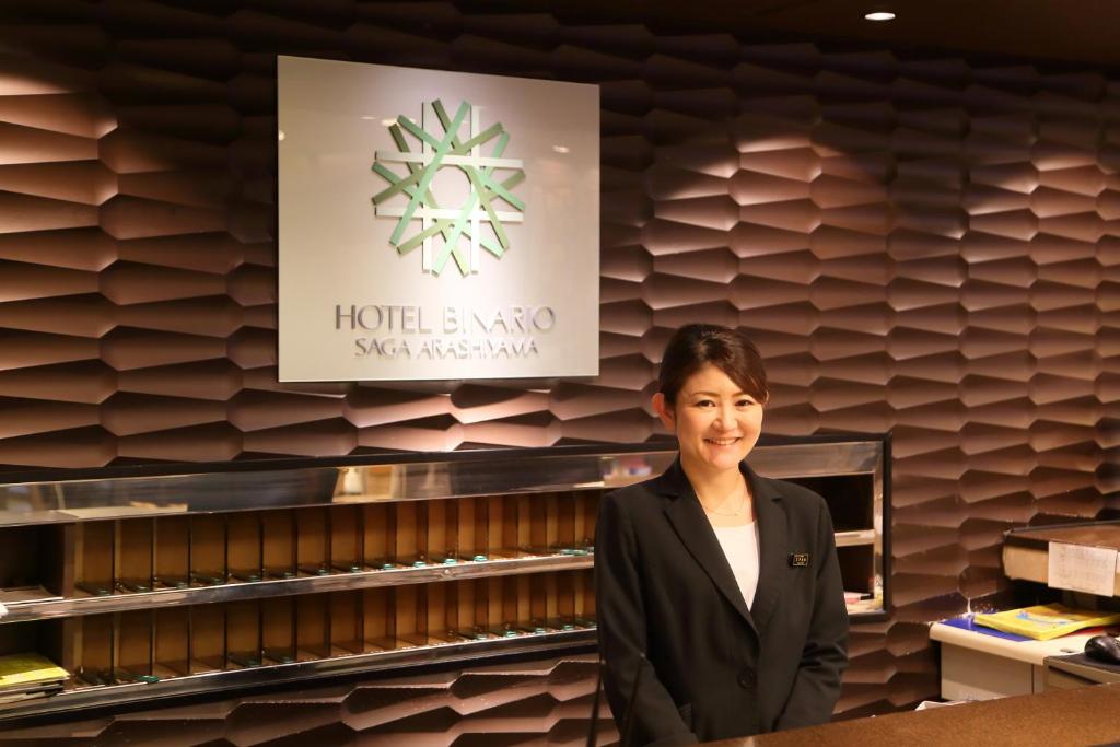 a woman standing in a restaurant with a sign on the wall at Hotel Binario Saga Arashiyama in Kyoto