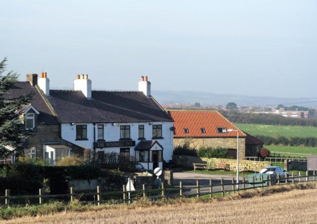 a white house with a fence next to a field at The Windmill Inn - Whitby in Whitby