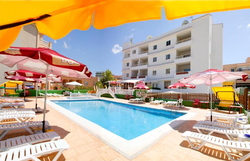 a pool with chairs and umbrellas next to a hotel at Apartamentos Vista al Puerto in San Antonio Bay