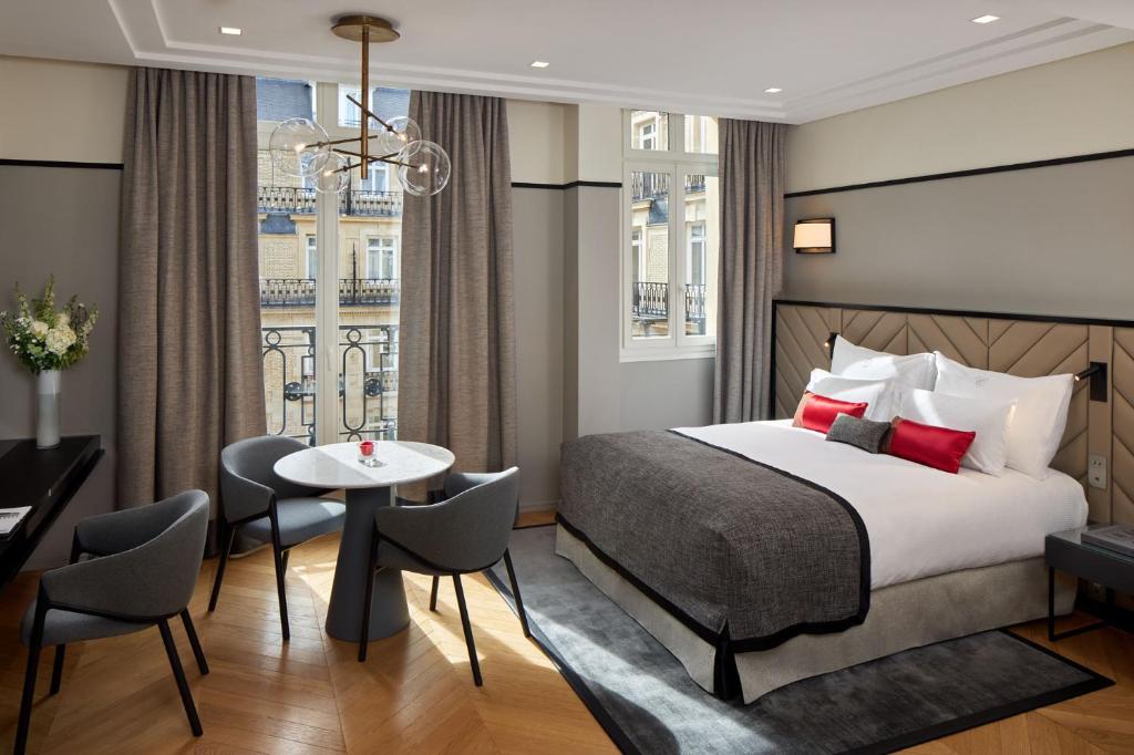 パリにあるフレイザー スイート ル クラリッジ シャンゼリゼのベッド、テーブル、椅子が備わるホテルルームです。