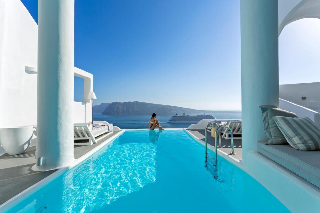 a woman standing next to a swimming pool with blue water at Charisma Suites in Oia