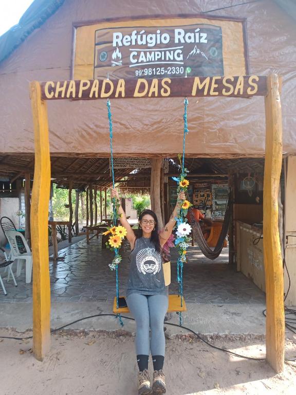 a woman sitting on a swing in front of a sign at Refúgio Raiz Camping in Carolina