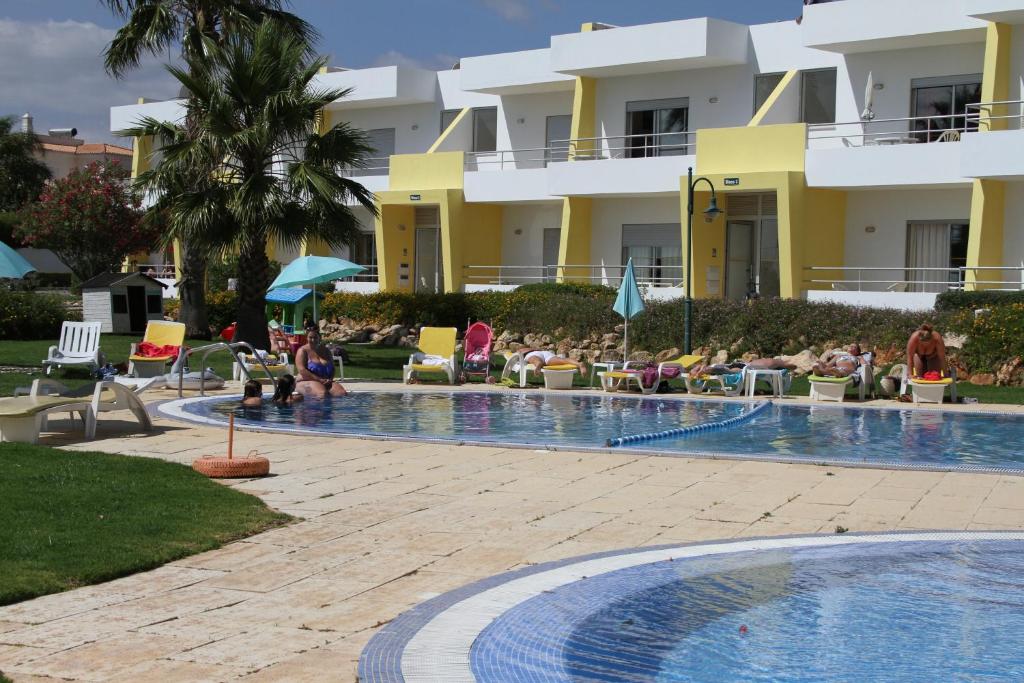 a resort with a swimming pool with people sitting in chairs at Apartamentos Santa Teresinha in Alvor