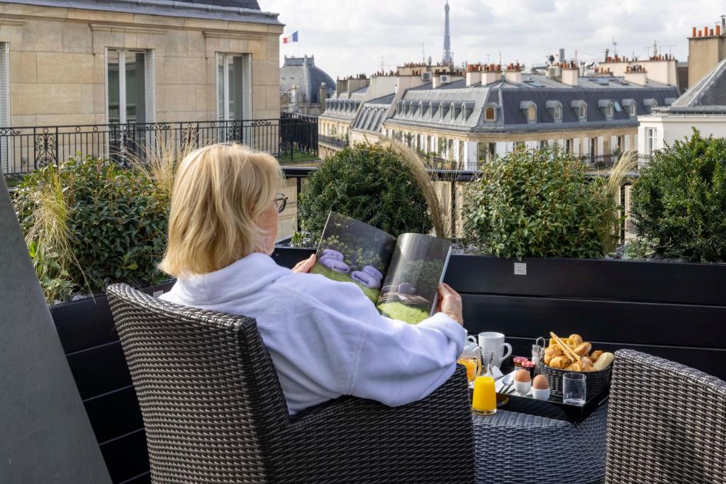 a woman sitting on a balcony reading a book at Le 12 Hôtel in Paris