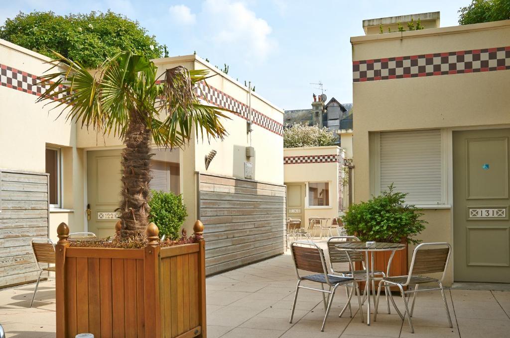 a patio with a table and chairs and a palm tree at Almoria Hôtel & SPA in Deauville