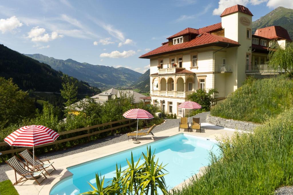 ein Haus mit einem Pool und zwei Sonnenschirmen in der Unterkunft Villa Excelsior Hotel & Kurhaus in Bad Gastein