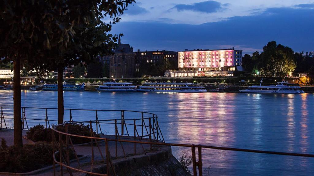 Un río con barcos en una ciudad por la noche en AMERON Bonn Hotel Königshof, en Bonn