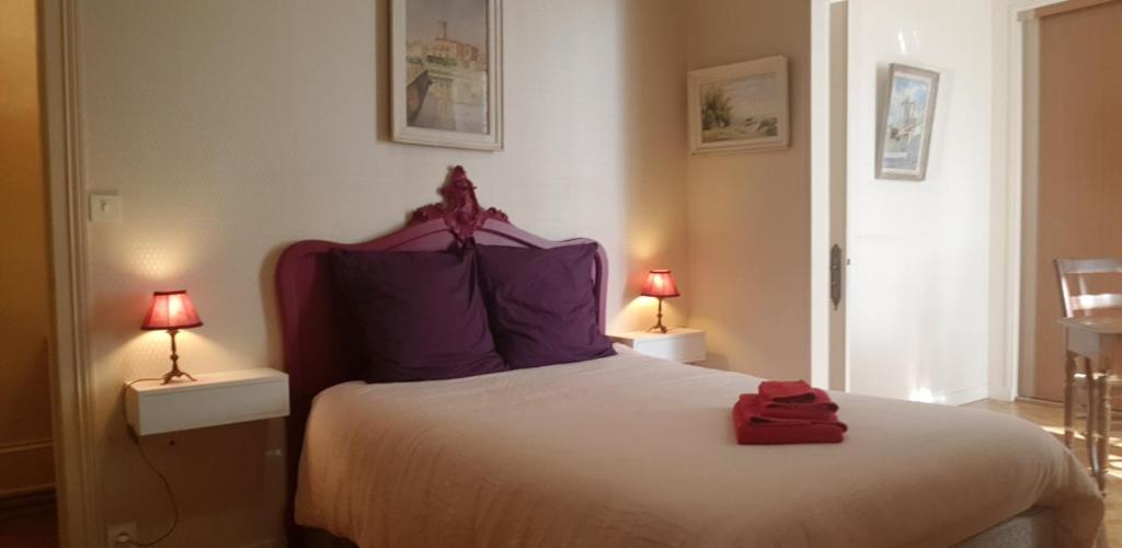 een slaapkamer met een bed met paarse kussens en 2 lampen bij La maison de Louise in Fontenay-le-Comte