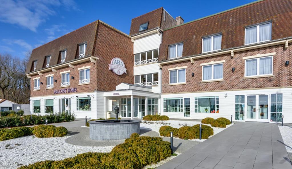 ein großes Backsteingebäude mit einem Brunnen davor in der Unterkunft Ara Dune Hotel in De Panne