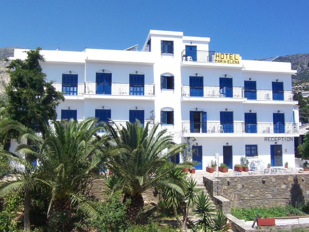 a white building with palm trees in front of it at Hotel Maria-Elena in Agios Kirykos