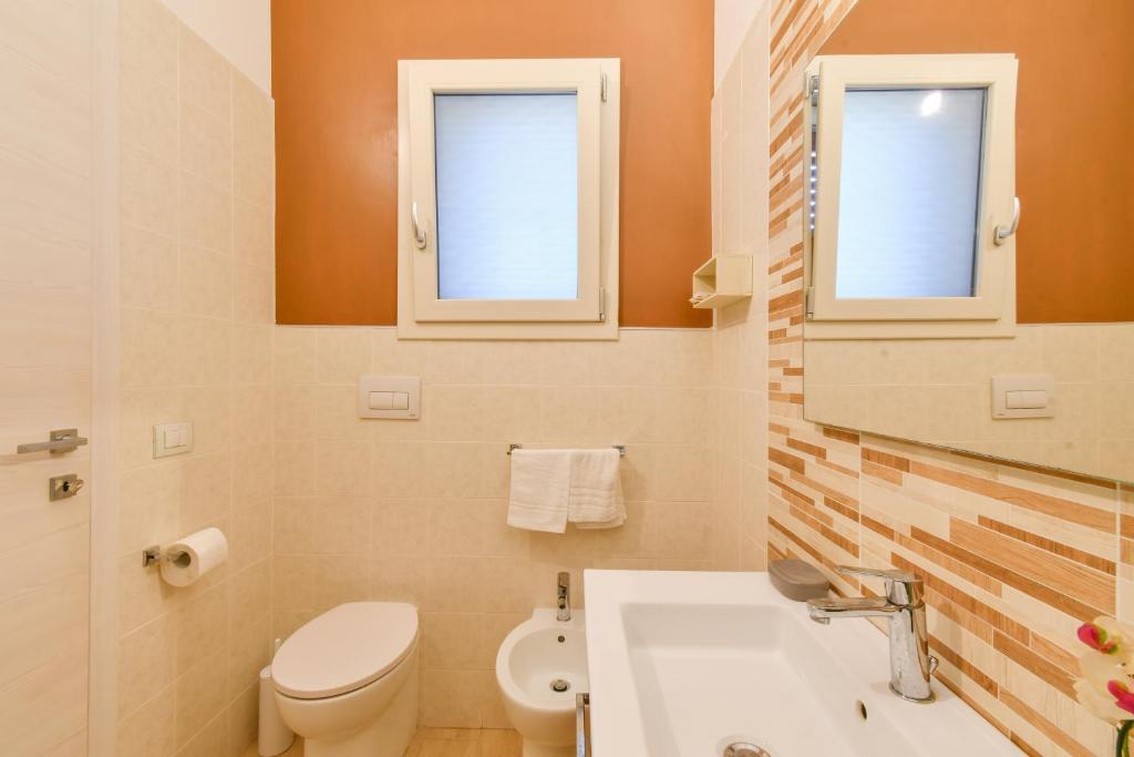 a bathroom with a toilet and a sink and two windows at Calasole Country House in Torre Lapillo