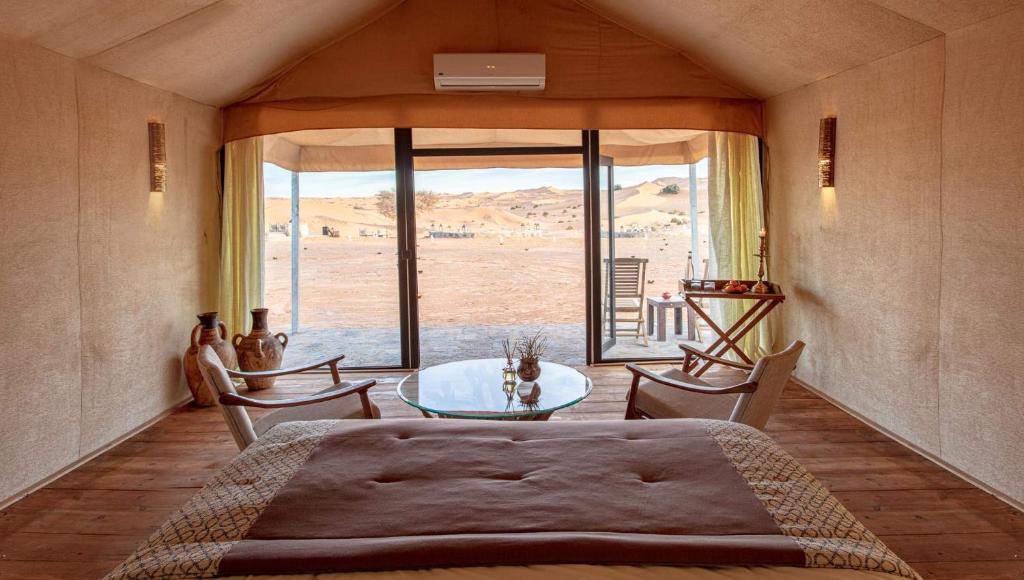 a bedroom with a table and chairs and a large window at Erg Chebbi Luxury Desert Camp in Merzouga