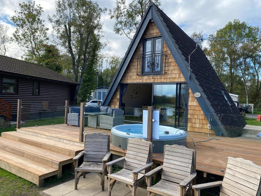 ein Haus mit einem Pool und Stühlen auf einer Terrasse in der Unterkunft Widgeon Bespoke Cabin is lakeside with Private fishing peg, hot tub situated at Tattershall Lakes Country Park in Tattershall